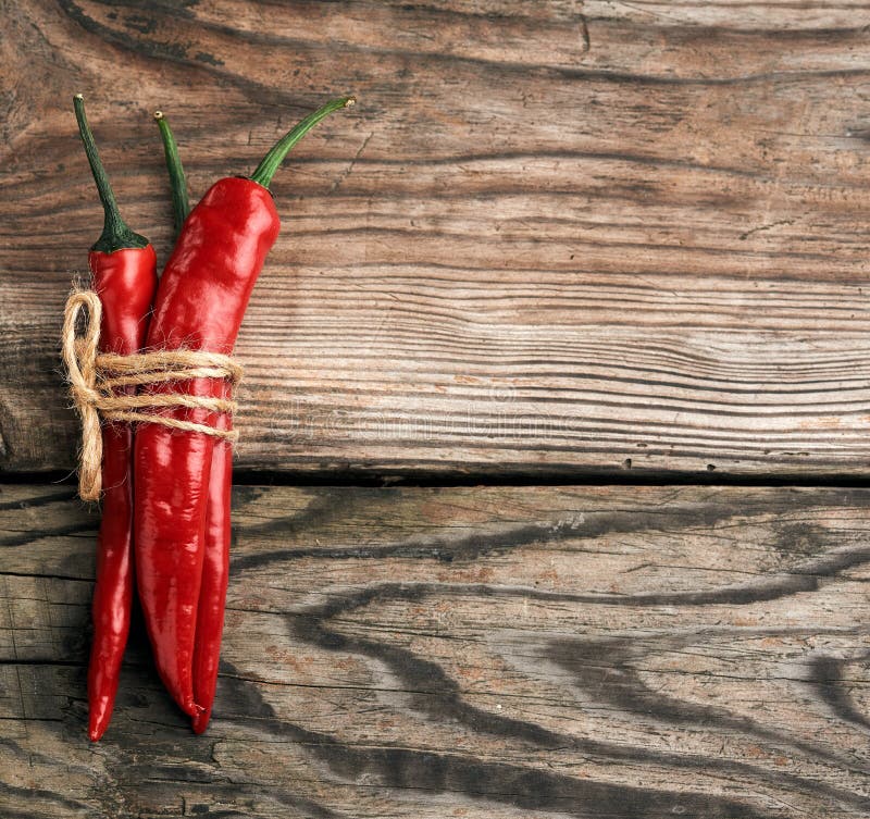 Pods of red chili peppers tied with a brown rope on a gray wooden background