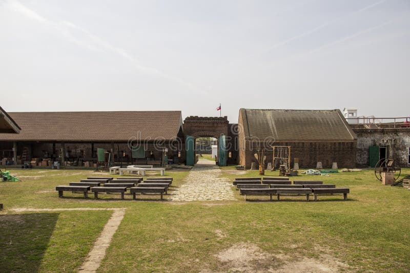 The courtyard of a military fort with brown wooden pergolas, brown wooden tables and benches and tools and equipment on the grass at Old Fort Jackson in Savannah Georgia USA. The courtyard of a military fort with brown wooden pergolas, brown wooden tables and benches and tools and equipment on the grass at Old Fort Jackson in Savannah Georgia USA