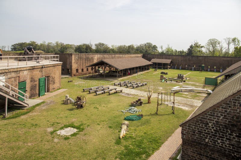 The courtyard of a military fort with brown wooden pergolas, brown wooden tables and benches and tools and equipment on the grass at Old Fort Jackson in Savannah Georgia USA. The courtyard of a military fort with brown wooden pergolas, brown wooden tables and benches and tools and equipment on the grass at Old Fort Jackson in Savannah Georgia USA