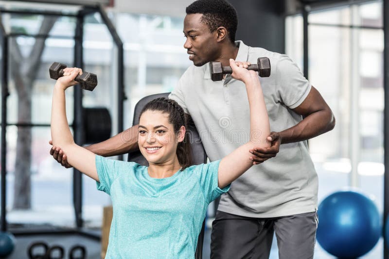 Poids de levage de femme sportive aidés par l'entraîneur photo libre de droits Poids de levage de femme sportive aidés par l'entraîneur photo libre de droits