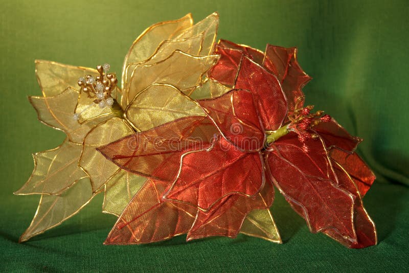 Two poinsettias. One red and one gold on a green textile. Two poinsettias. One red and one gold on a green textile