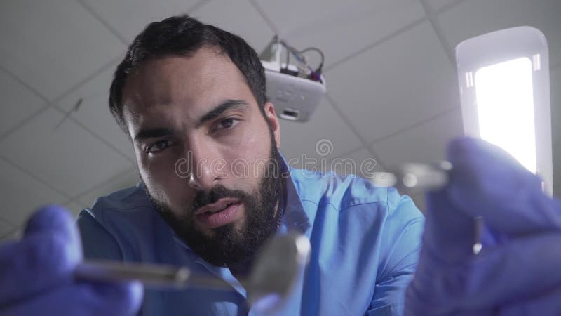 Point de vue patient du dentiste du Moyen-Orient beau manipulant. Portrait de stomatologist mâle sûr sérieux banque de vidéos