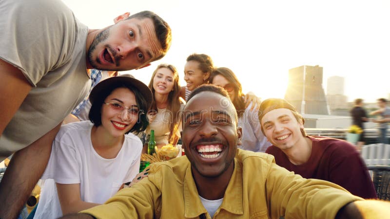 Point of view shot of young people multiethnic group taking selfie and holding camera, men and women are looking at