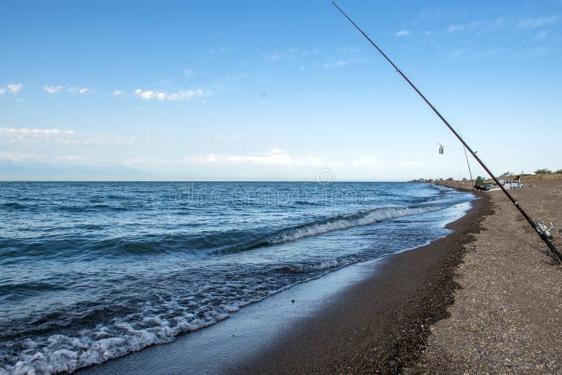 Poissons de pêcheur tôt le matin sur le rivage Canne à pêche et rotation camper image stock Poissons de pêcheur tôt le matin sur le rivage Canne à pêche et rotation camper image stock