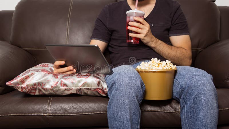 Pojedynczy mężczyzna ogląda film na cyfrowej pastylce Pije sok