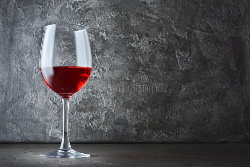 Single glass of red wine for tasting in dark cellar with copy space on gray concrete background. Single glass of red wine for tasting in dark cellar with copy space on gray concrete background