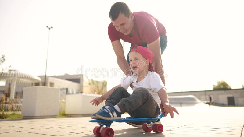 Pojk lär sig att skateboard. Pappa lär son att åka på ett skateboard utomhus på lekplatsen. fader och pojkens livsstil. Pappa undervisar son att åka skateboard utomhus på lekplatsen. Fader och pojkars livsstil spelar träningskoncept. moderundervisande underordnad son till skateboard.