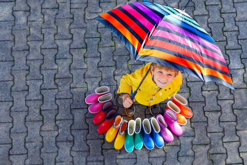 Pojke f?r liten unge och grupp av f?rgrika regnk?ngor Blont barnanseende under paraplyet N?rbild av skolbarnet och arkivfoto Pojke f?r liten unge och grupp av f?rgrika regnk?ngor Blont barnanseende under paraplyet N?rbild av skolbarnet och arkivfoto