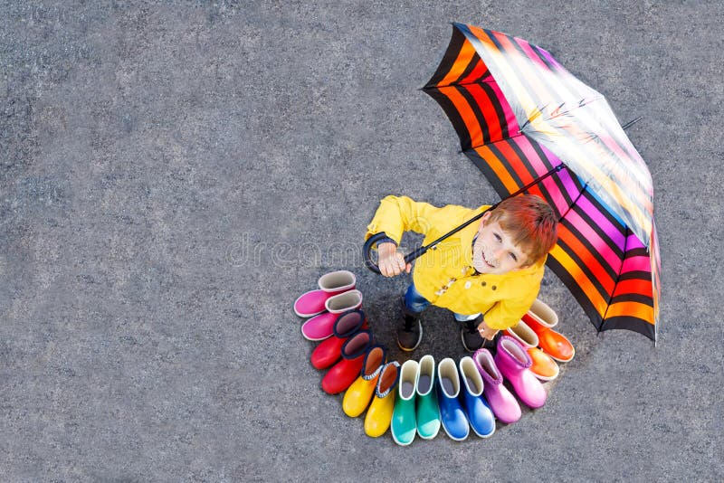 Pojke för liten unge och grupp av färgrika regnkängor Blont barnanseende under paraplyet arkivfoto Pojke för liten unge och grupp av färgrika regnkängor Blont barnanseende under paraplyet arkivfoto