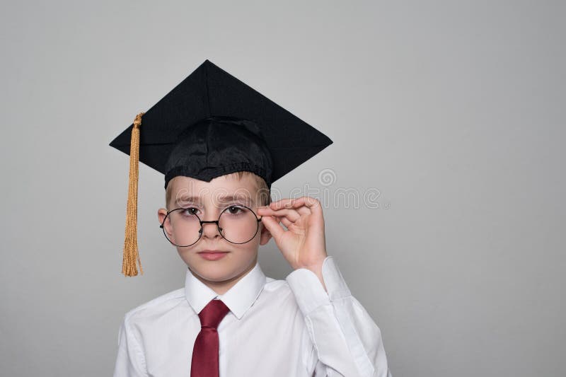 Pojke i ett fyrkantigt akademiskt lock och en vit skjorta som korrigerar exponeringsglas Vit bakgrund skola f?r copyspace f?r beg royaltyfri foto Pojke i ett fyrkantigt akademiskt lock och en vit skjorta som korrigerar exponeringsglas Vit bakgrund skola f?r copyspace f?r beg royaltyfri foto