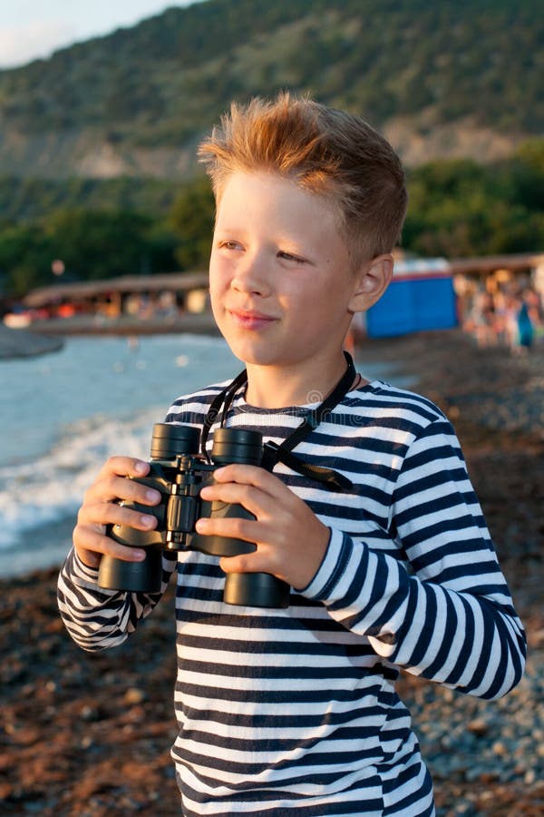 Pojke i garnisonlock och randigt västanseende nära havet med royaltyfri fotografi Pojke i garnisonlock och randigt västanseende nära havet med royaltyfri fotografi