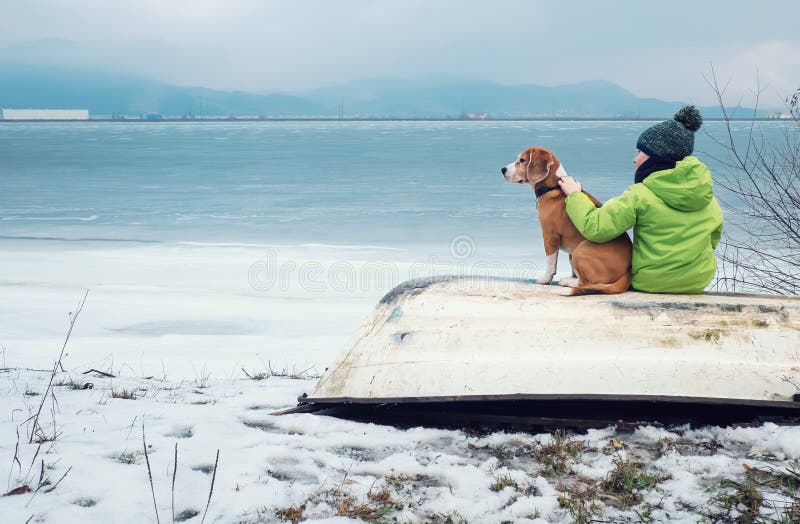 Pojke med hunden som tillsammans sitter på den near vintersjön för gammalt fartyg royaltyfri bild Pojke med hunden som tillsammans sitter på den near vintersjön för gammalt fartyg royaltyfri bild