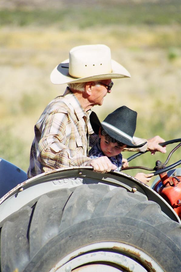 A little boy riding a tractor with his great grandfather older man farmer. A little boy riding a tractor with his great grandfather older man farmer