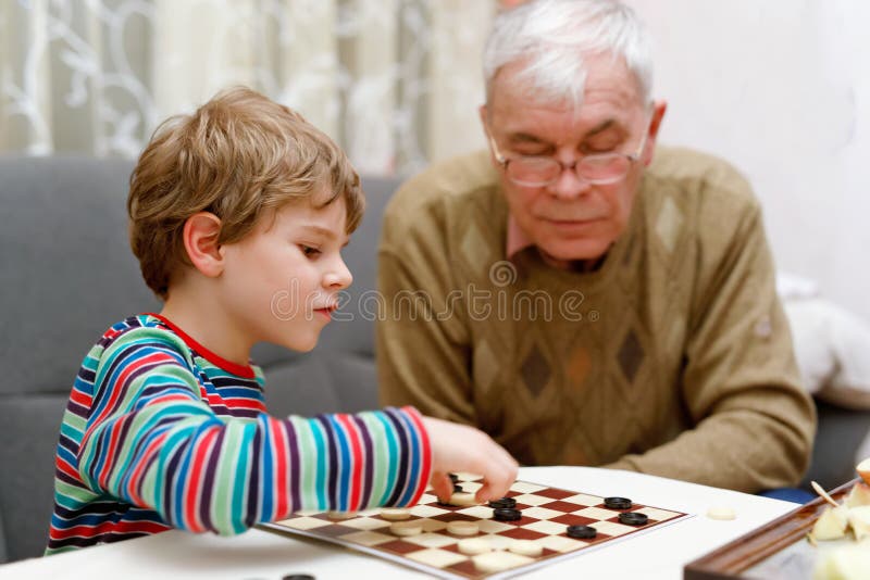 Дед с внуком играют в шашки. Дедушка играет в шашки. Дед и внук играют в шахматы. Мальчик играет в шахматы с дедом.