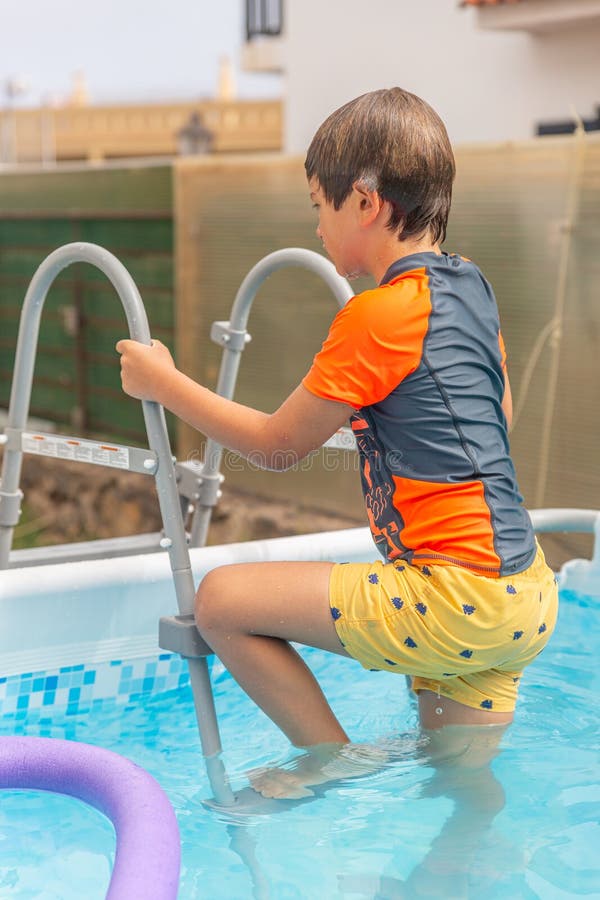 Pojken fokuserade på att klättra ut ur en pool med hjälp av stegen och visa försiktighet och roligt royaltyfri foto