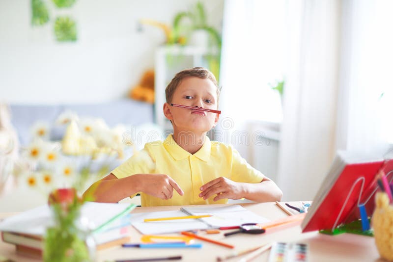 Pojken g?r hans l?xa hemma lyckligt barn på tabellen med näsan för leenden och för skrynklor för skolatillförsel den roliga royaltyfria foton Pojken g?r hans l?xa hemma lyckligt barn på tabellen med näsan för leenden och för skrynklor för skolatillförsel den roliga royaltyfria foton