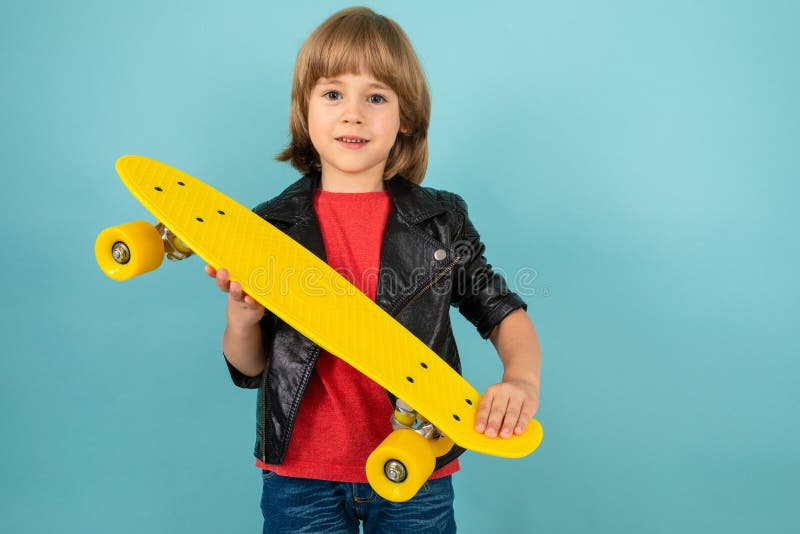 Pojken håller gul skateboard i händerna på en blå bakgrund royaltyfria foton