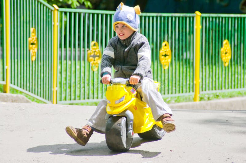 Pojken på sparkcykeln. Tre åriga pojkeritter på leksaksparkcykeln Vårsäsongen Han bär en rolig hatt i formen av en fisk