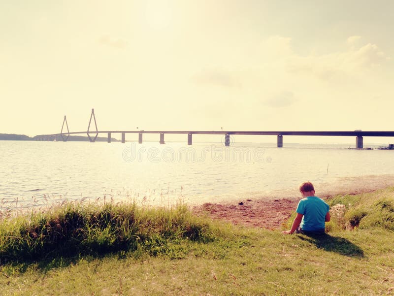Pojken spelar leken på frånlands-, sikt till den stora trafikbron över fjärden Bron för två väg med höga torn royaltyfria foton Pojken spelar leken på frånlands-, sikt till den stora trafikbron över fjärden Bron för två väg med höga torn royaltyfria foton