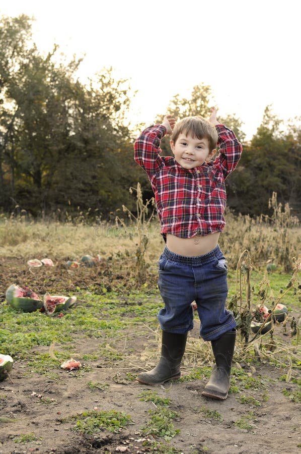 Smiling boy standing in a watermelon patch, raising his hands and showing his belly button. Smiling boy standing in a watermelon patch, raising his hands and showing his belly button