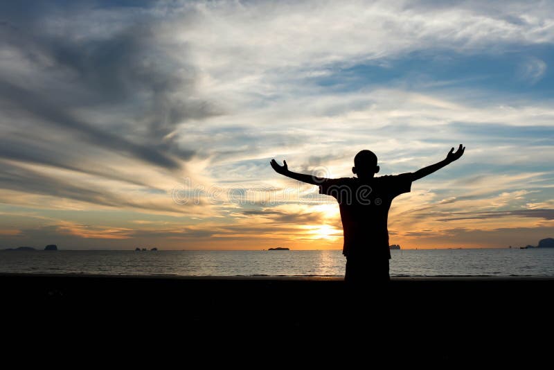 Silhouette of a boy with hands raised on a beach at the sunset concept for religion, worship, prayer and praise. Silhouette of a boy with hands raised on a beach at the sunset concept for religion, worship, prayer and praise.