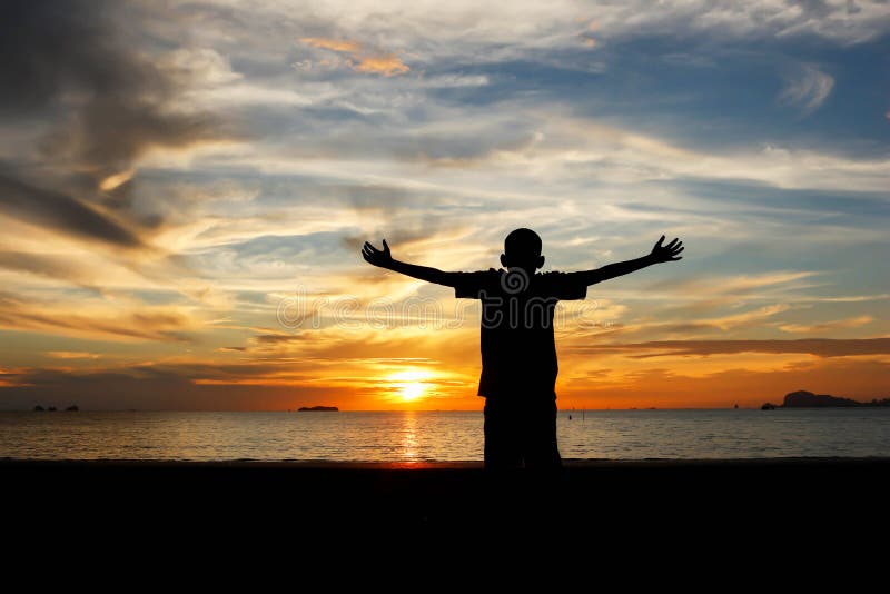Silhouette of a boy with hands raised on a beach at the sunset concept for religion, worship, prayer and praise. Silhouette of a boy with hands raised on a beach at the sunset concept for religion, worship, prayer and praise.