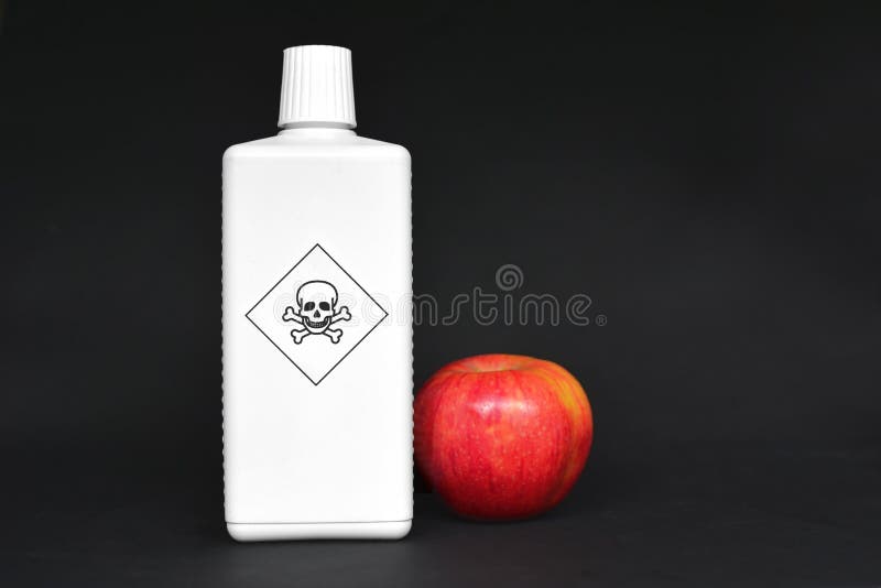 Concept for usage of dangerous pesticides in agricultural food products. Red apple standing next to white bottle with poisonous warning label with skull on black background. Concept for usage of dangerous pesticides in agricultural food products. Red apple standing next to white bottle with poisonous warning label with skull on black background