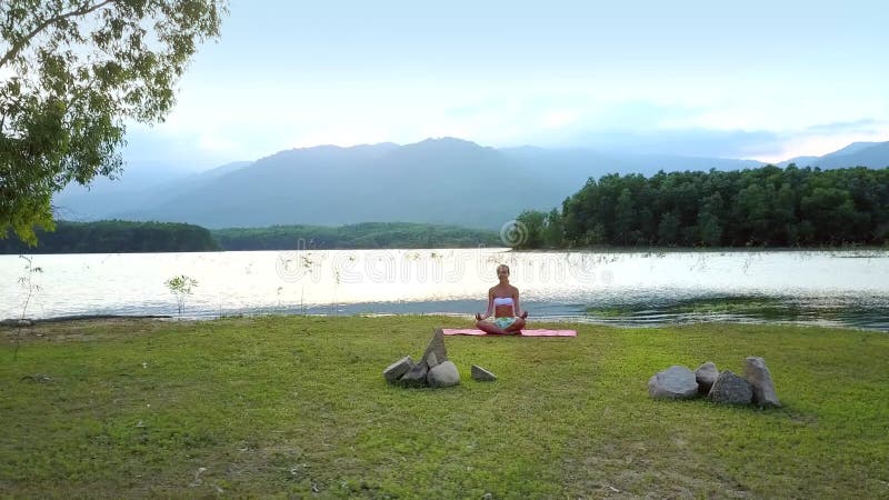 Pokojowa obrazek dziewczyna siedzi w lotos pozie na spokojnym jeziornym banku
