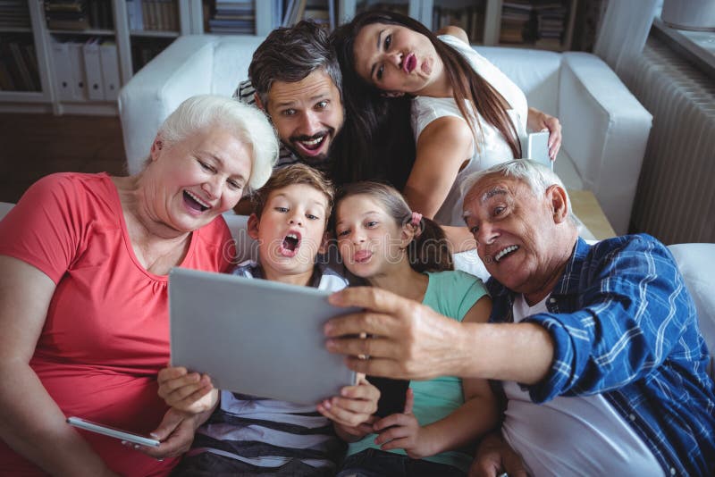 Multi-generation family taking a selfie on digital tablet in living room at home. Multi-generation family taking a selfie on digital tablet in living room at home
