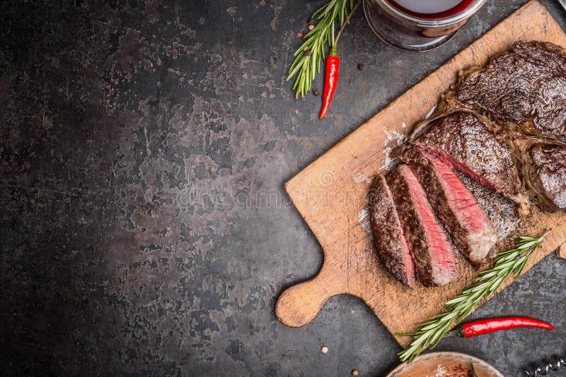 Pokrojony średni rzadki piec na grillu stek na nieociosanej tnącej desce z rozmarynami i pikantność zdjęcie stock