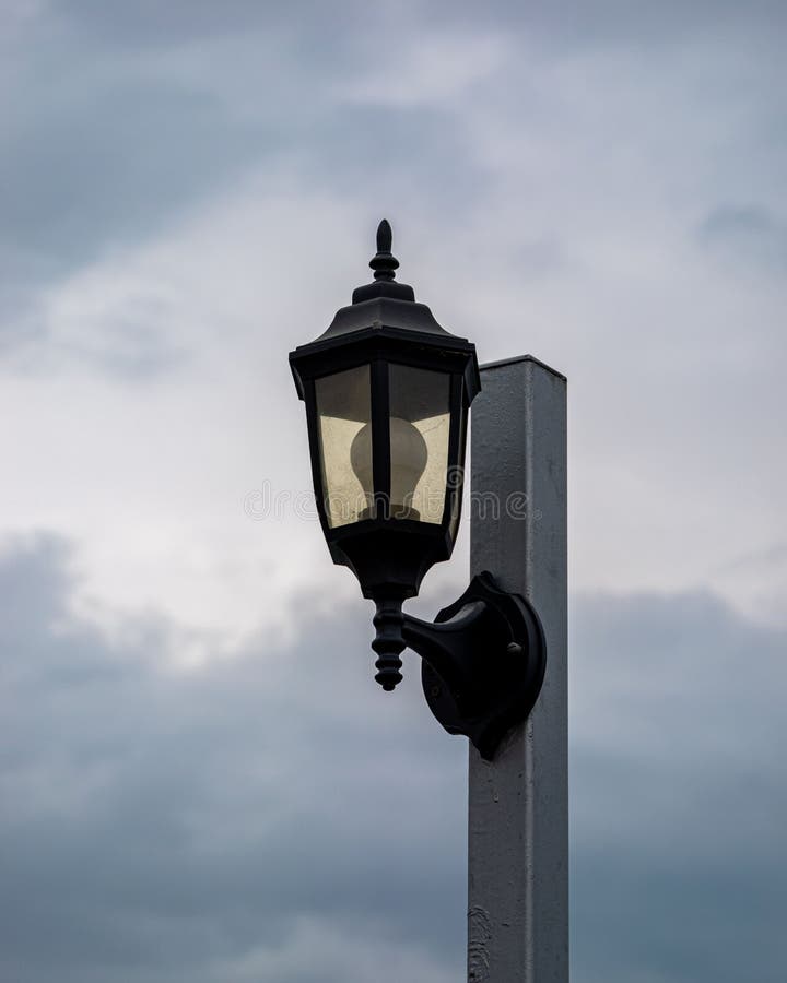Pole with Lightbulb Against Dramatic Gray Sky, Vertical Shot Stock