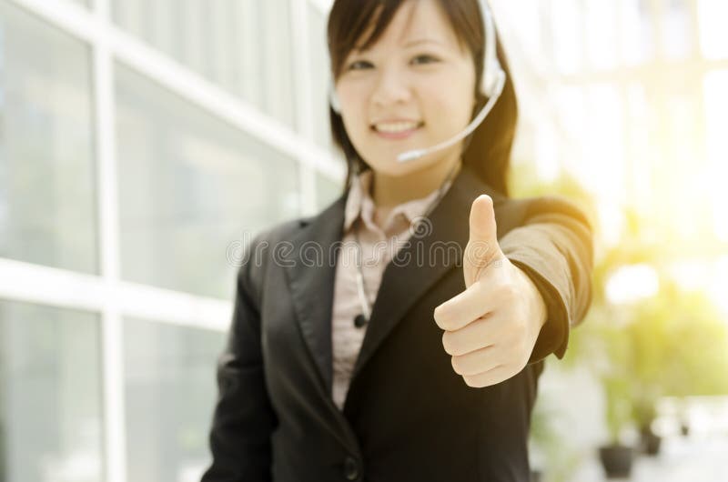 Polegar fêmea asiático do recepcionista acima imagens de stock royalty free Polegar fêmea asiático do recepcionista acima imagens de stock royalty free