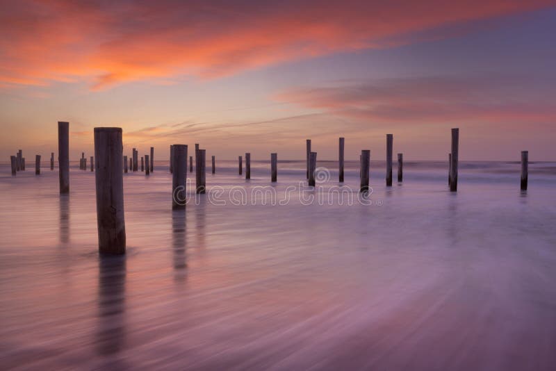 Poli di legno sulla spiaggia al tramonto immagine stock Poli di legno sulla spiaggia al tramonto immagine stock