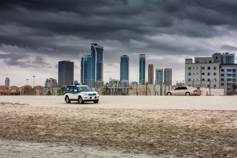 Police off-road car and city sedan on a sandy beach in the background of skyscrapers in cloudy weather