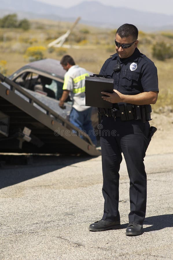 Police Officer Writing Notes At Car Crash Scene