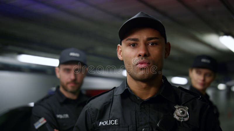 Policeman posing at camera. Police officer in cap standing at patrol car. African policeman with serious face posing at camera. Brutal police officer in cap