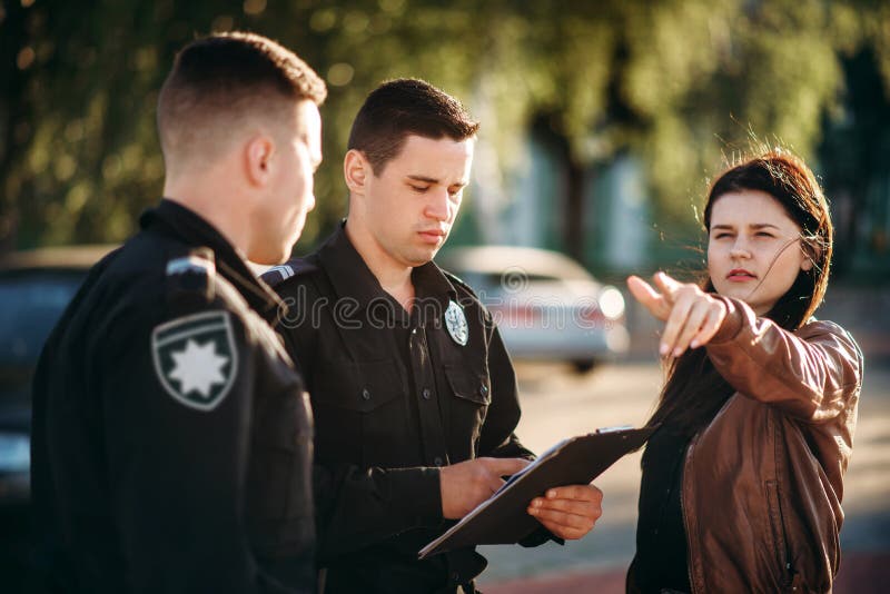 Polisen skriver vittnesbörd av den kvinnliga chauffören royaltyfri fotografi Polisen skriver vittnesbörd av den kvinnliga chauffören royaltyfri fotografi