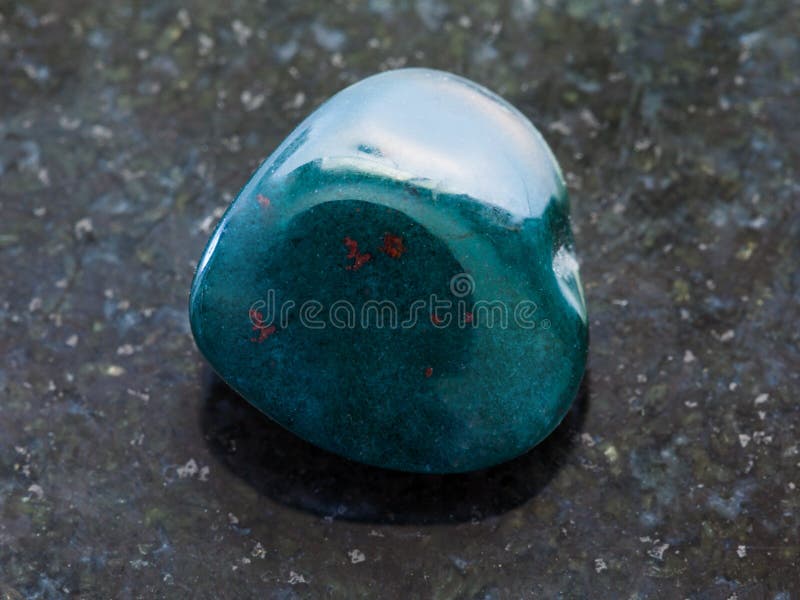 macro shooting of natural mineral rock specimen - polished heliotrope gemstone on dark granite background. macro shooting of natural mineral rock specimen - polished heliotrope gemstone on dark granite background