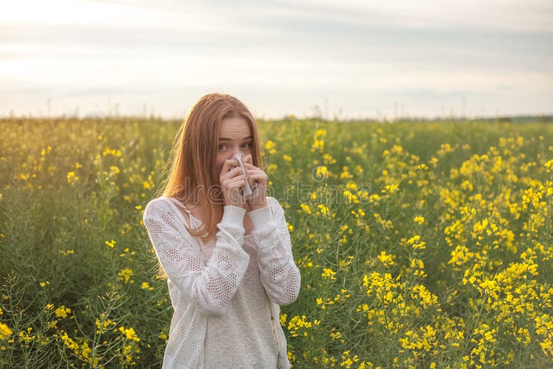 Pollen allergy, girl sneezing in a rapeseed field of flowers