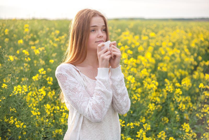 Pollen allergy, girl sneezing in a rapeseed field of flowers.