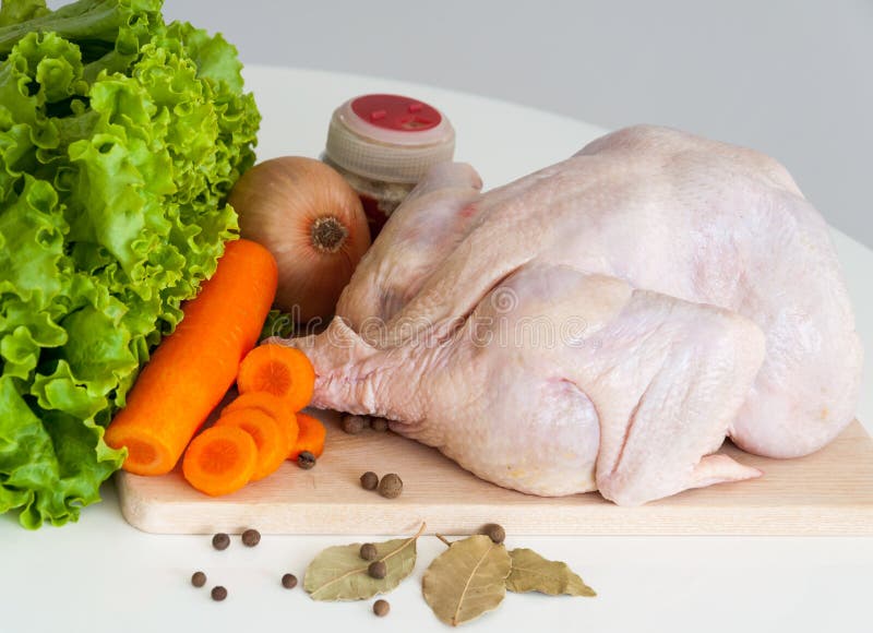 Whole raw chicken with vegetables and a bottle of spices on a cutting board. Whole raw chicken with vegetables and a bottle of spices on a cutting board