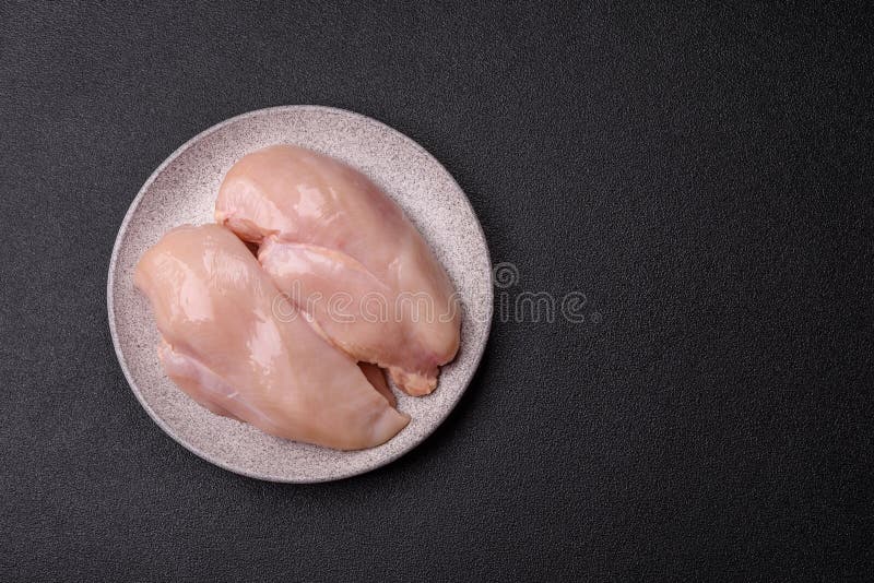 Pollo crudo o filete de pavo con especias saladas y hierbas en un fondo de hormigón oscuro