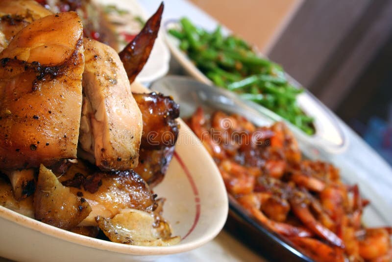 A plate of roasted chicken spread on the dinner table with prawns and vegetables in the background. A plate of roasted chicken spread on the dinner table with prawns and vegetables in the background.