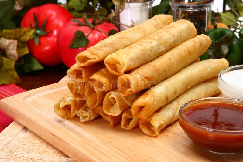 Stack of chicken taquitos with hot sauce and sour cream in kitchen or restaurant. Stack of chicken taquitos with hot sauce and sour cream in kitchen or restaurant