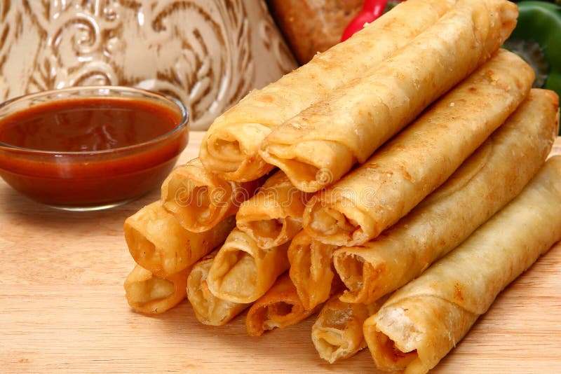 Stack of chicken taquitos with hot sauce and sour cream in kitchen or restaurant. Stack of chicken taquitos with hot sauce and sour cream in kitchen or restaurant