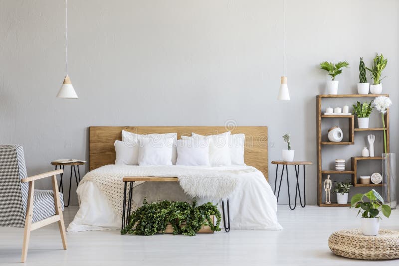 Poltrona modellata vicino al letto di legno bianco nell'interno grigio della camera da letto con il pouf e le piante Foto reale