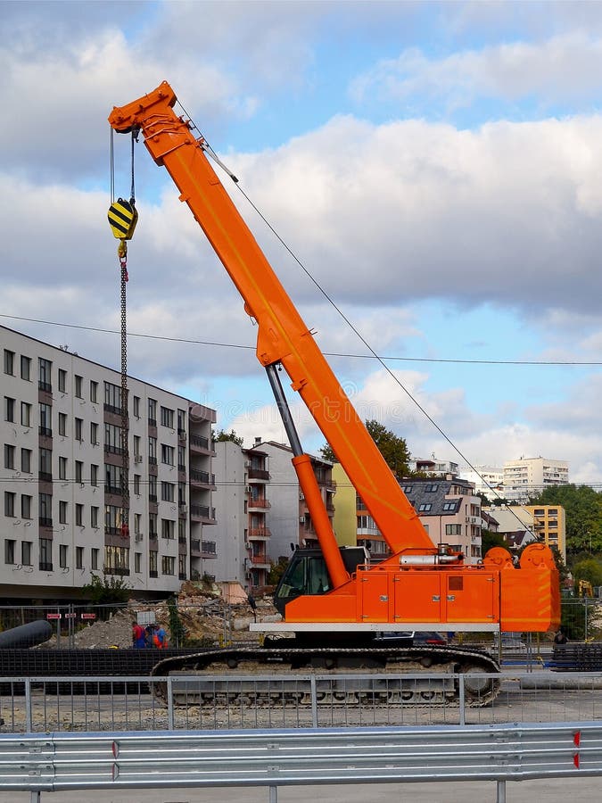 Pomarańczowy śpioszka żuraw przy miejscem budowa drogi pracuje w mieście przeciw tłu budynek mieszkalny i s zdjęcia stock Pomarańczowy śpioszka żuraw przy miejscem budowa drogi pracuje w mieście przeciw tłu budynek mieszkalny i s zdjęcia stock