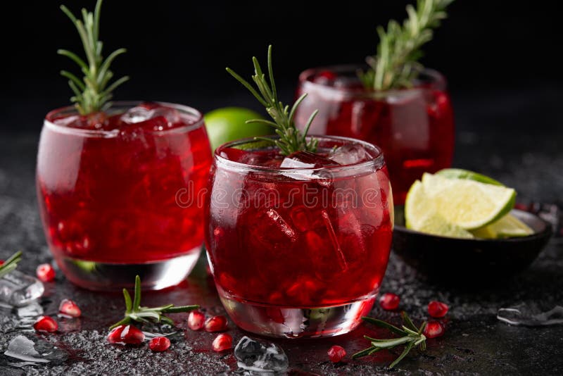 Pomegranate Gin Cocktail with Lime, Rosemary and Ice on Rustic Black