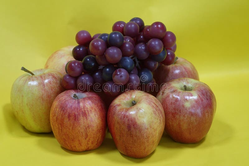Pommes et raisins violets disposés sur fond jaune photographie stock