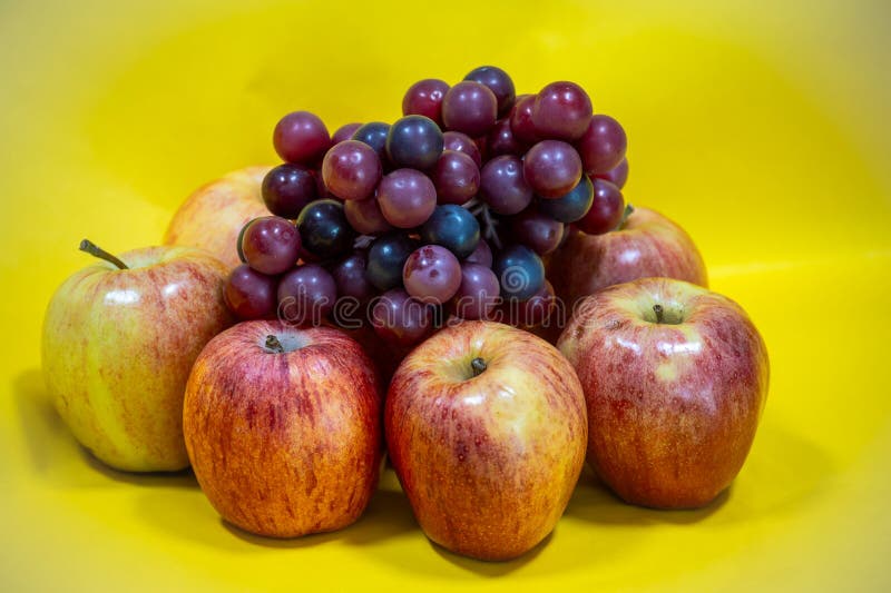 Pommes et raisins violets disposés sur fond jaune image libre de droits
